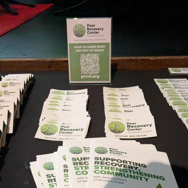 Peer Recovery Center of Addison County informational materials displayed on a table, including brochures, business cards and a QR code sign inviting visitors to learn more and stay in touch.